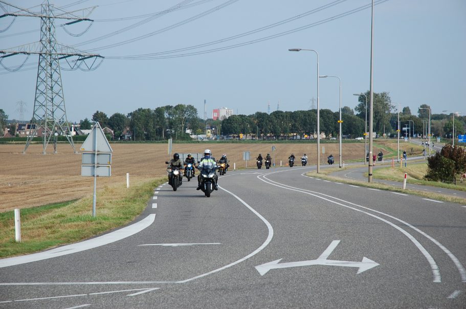 Voorrijder Marcel Twee motorrijders rijden op een bochtige weg naast een veld. Achtergrond met elektriciteitsmasten.